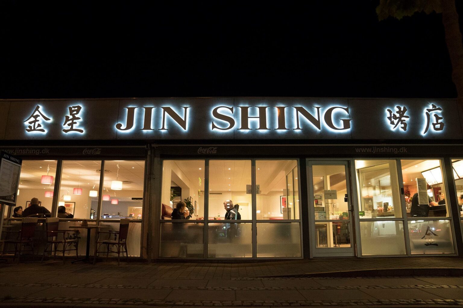 Jin Shing-facaden på Hjørringvej i Nørresundby ved aftenstid - oplyst neon-skilt med 'JIN SHING' og kinesiske skrifttegn 金星 og 烤店 over butiksvinduet